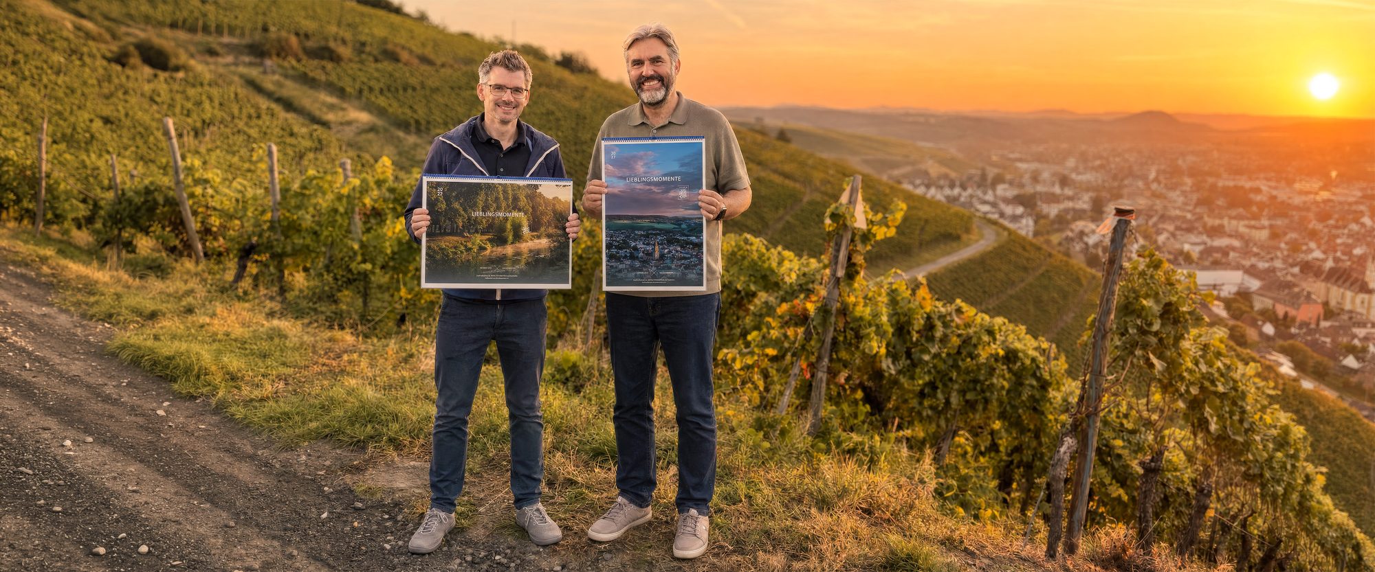 Kai Schneiders und ein zweiter Ahrtal-Fotograf halten die beiden Lieblingsmomente-Kalender 2027 in den Weinbergen über Bad Neuenahr-Ahrweiler bei Sonnenuntergang